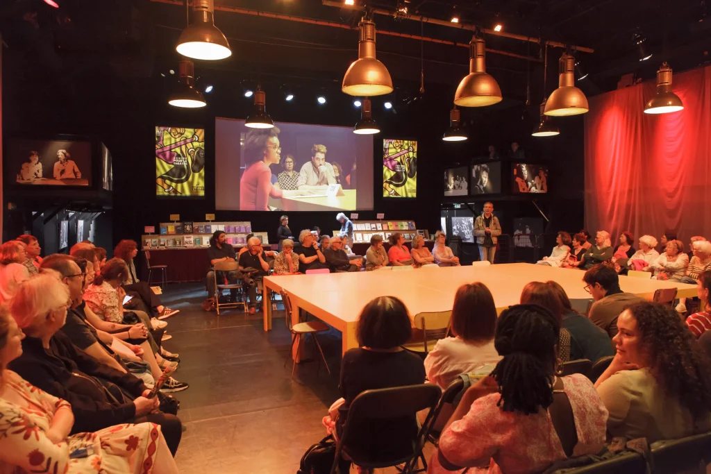 Le public autour des tables orange, en disposition quadrifrontale