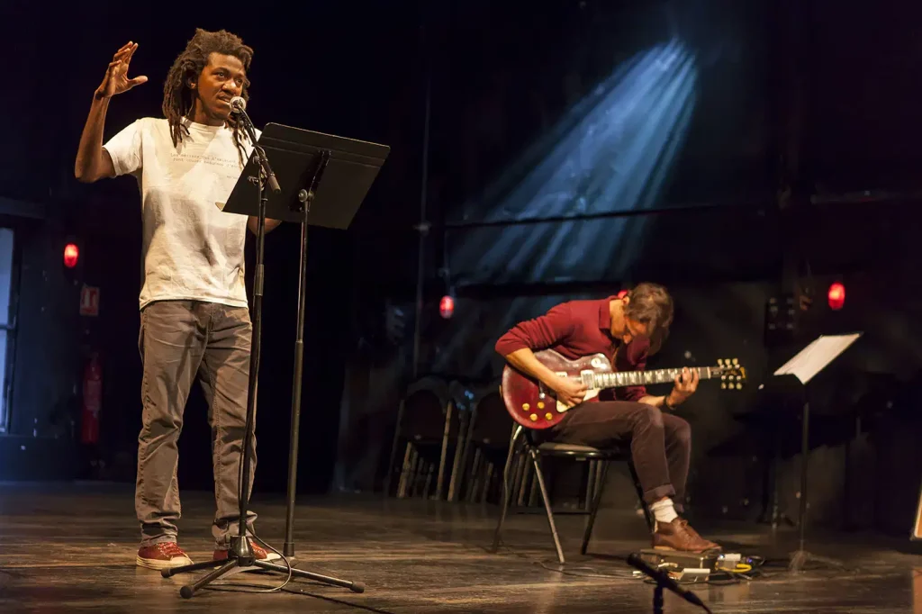 Jean d'Amérique déclamant son texte accompagné d'un musicien
